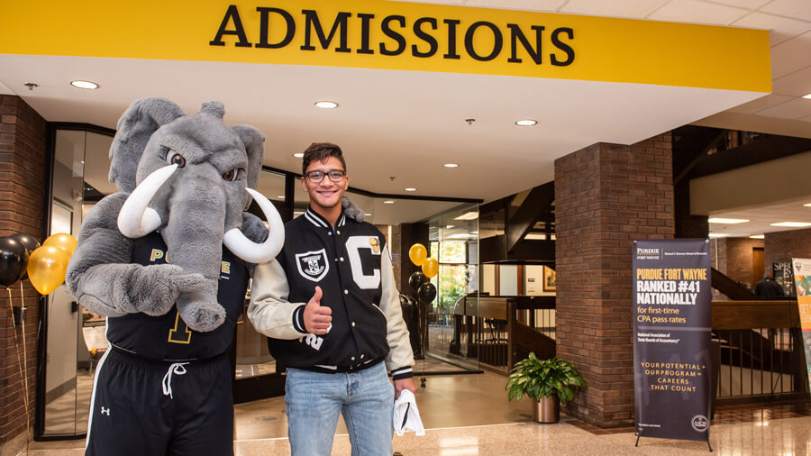 Don the Mastodon and a student give a thumbs up outside of the admissions office.